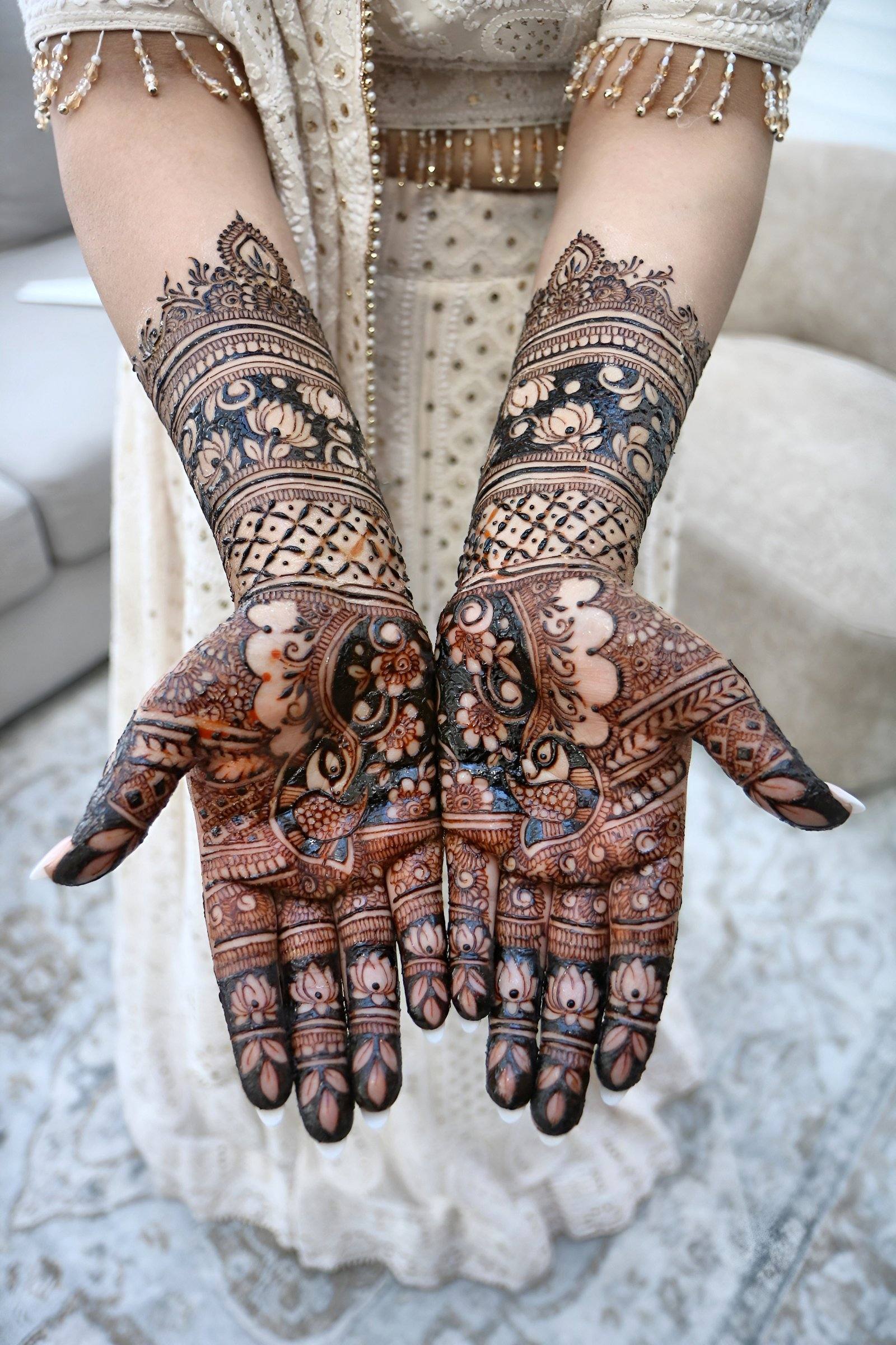 Bridal henna on both palms and forearms with floral and lattice detail over an ivory outfit