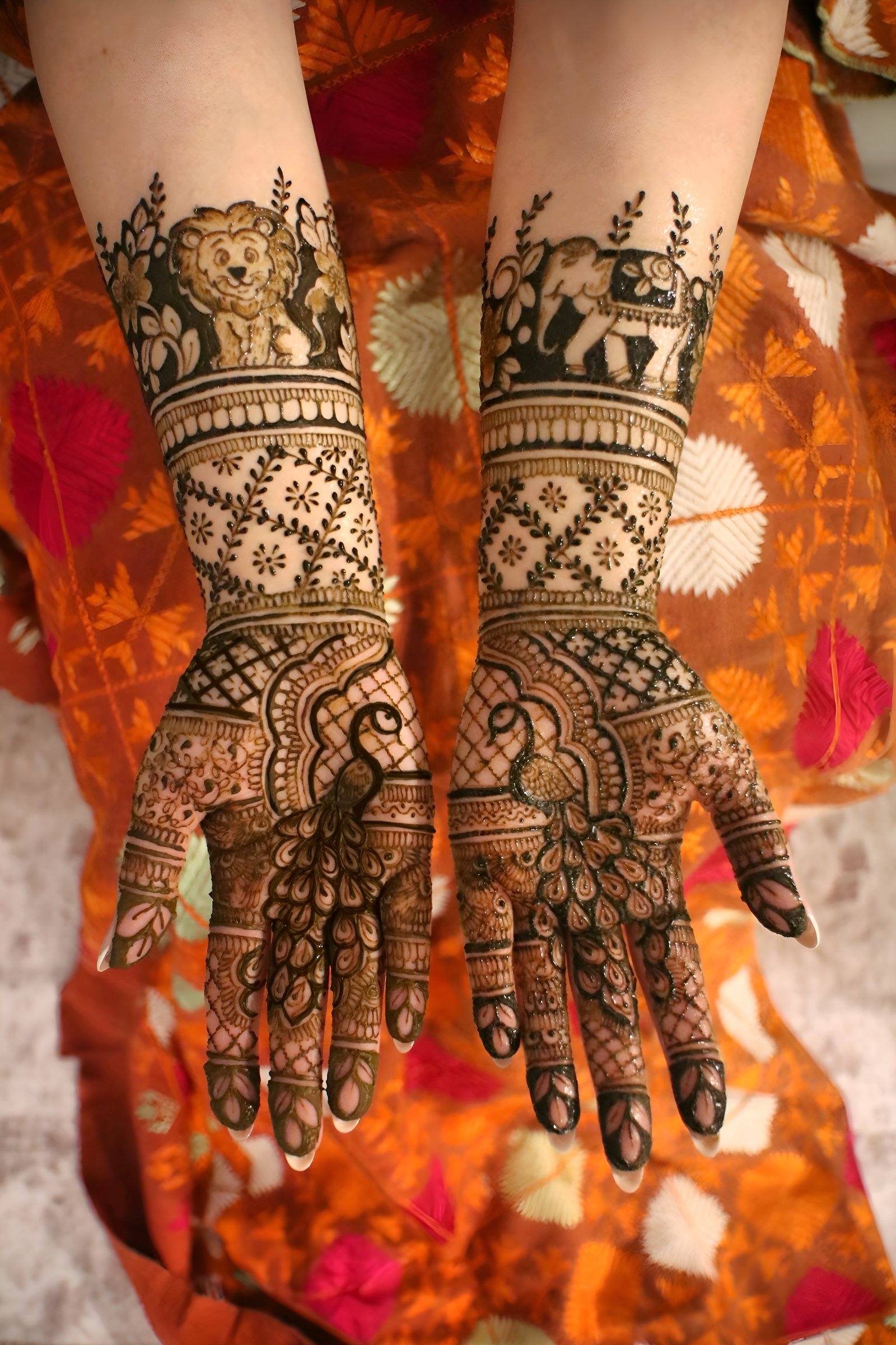 Bridal mehndi with lion and elephant motifs on arms over a bright orange phulkari dupatta