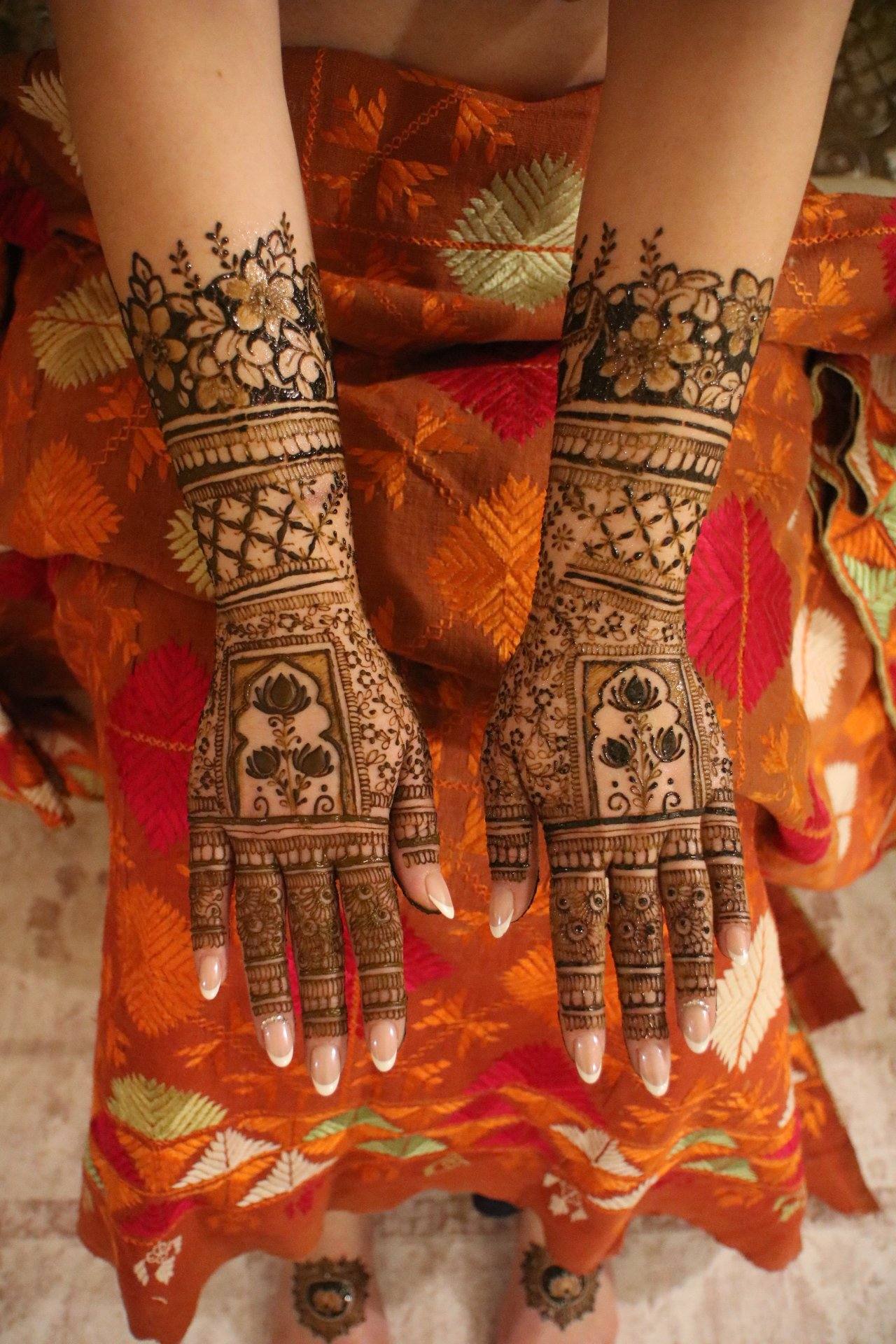 Floral bridal henna on the backs of the hands over an orange outfit