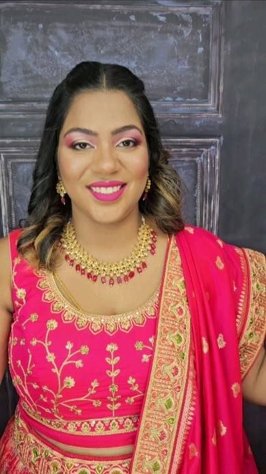 Smiling bride in a pink and gold outfit with gold necklace and bridal makeup