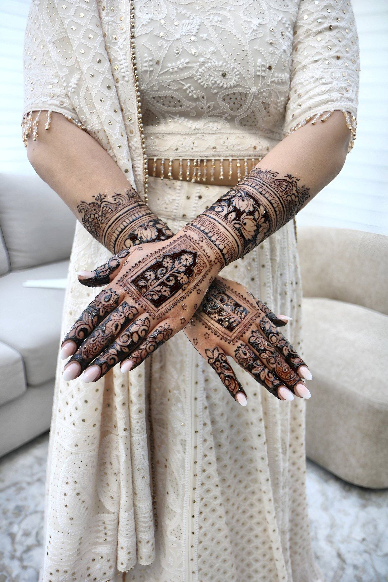Bride in ivory outfit crossing her henna-covered hands