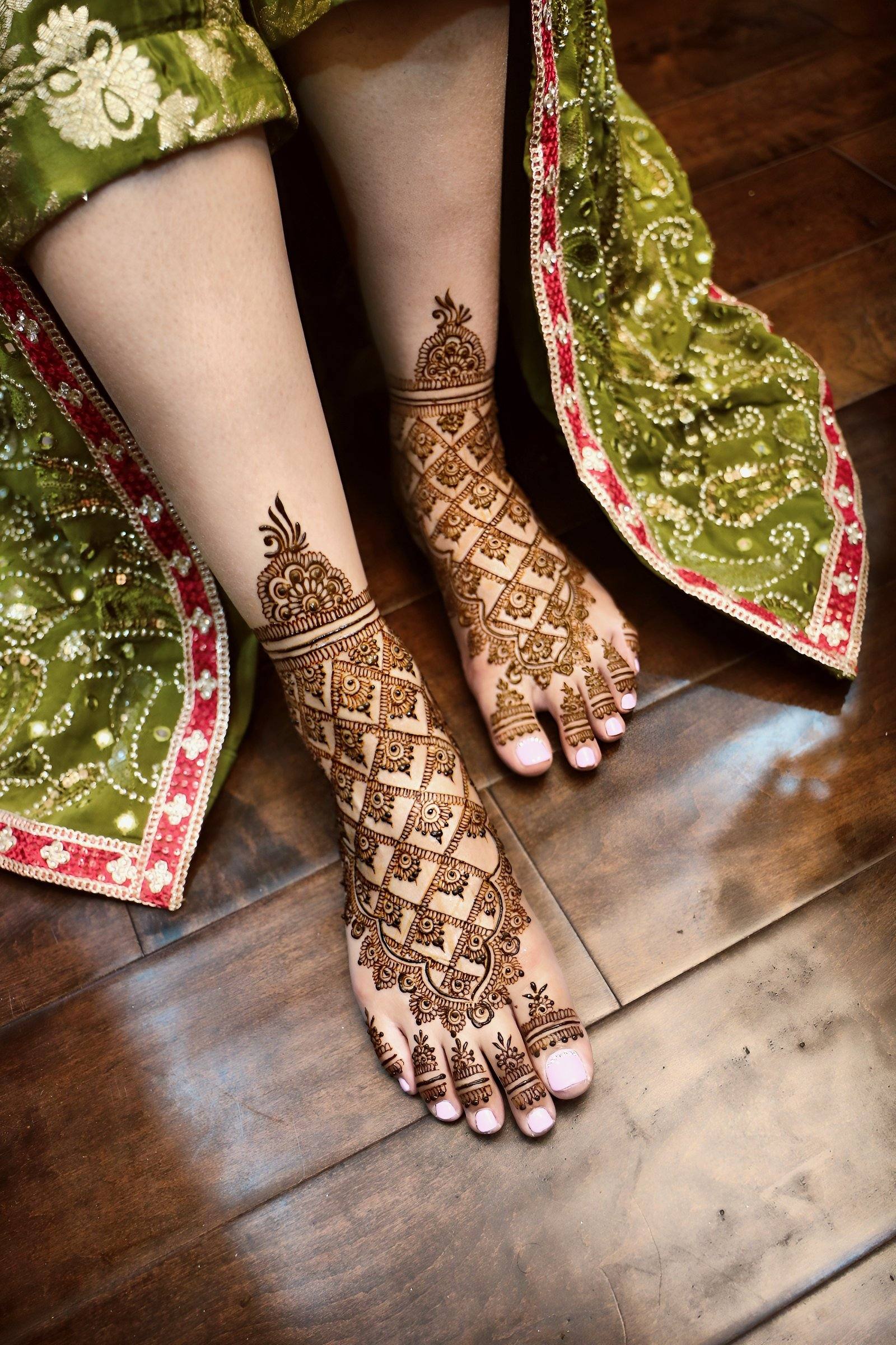 Bridal henna on feet beside a green and red lehenga