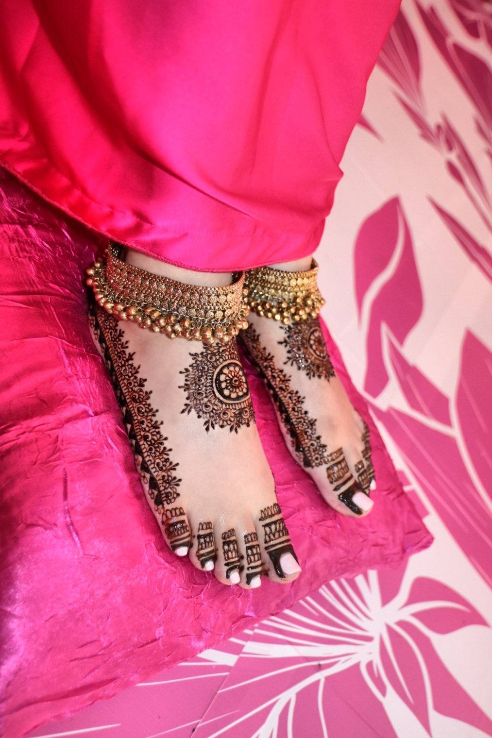 Bridal henna feet with gold anklets on pink fabric