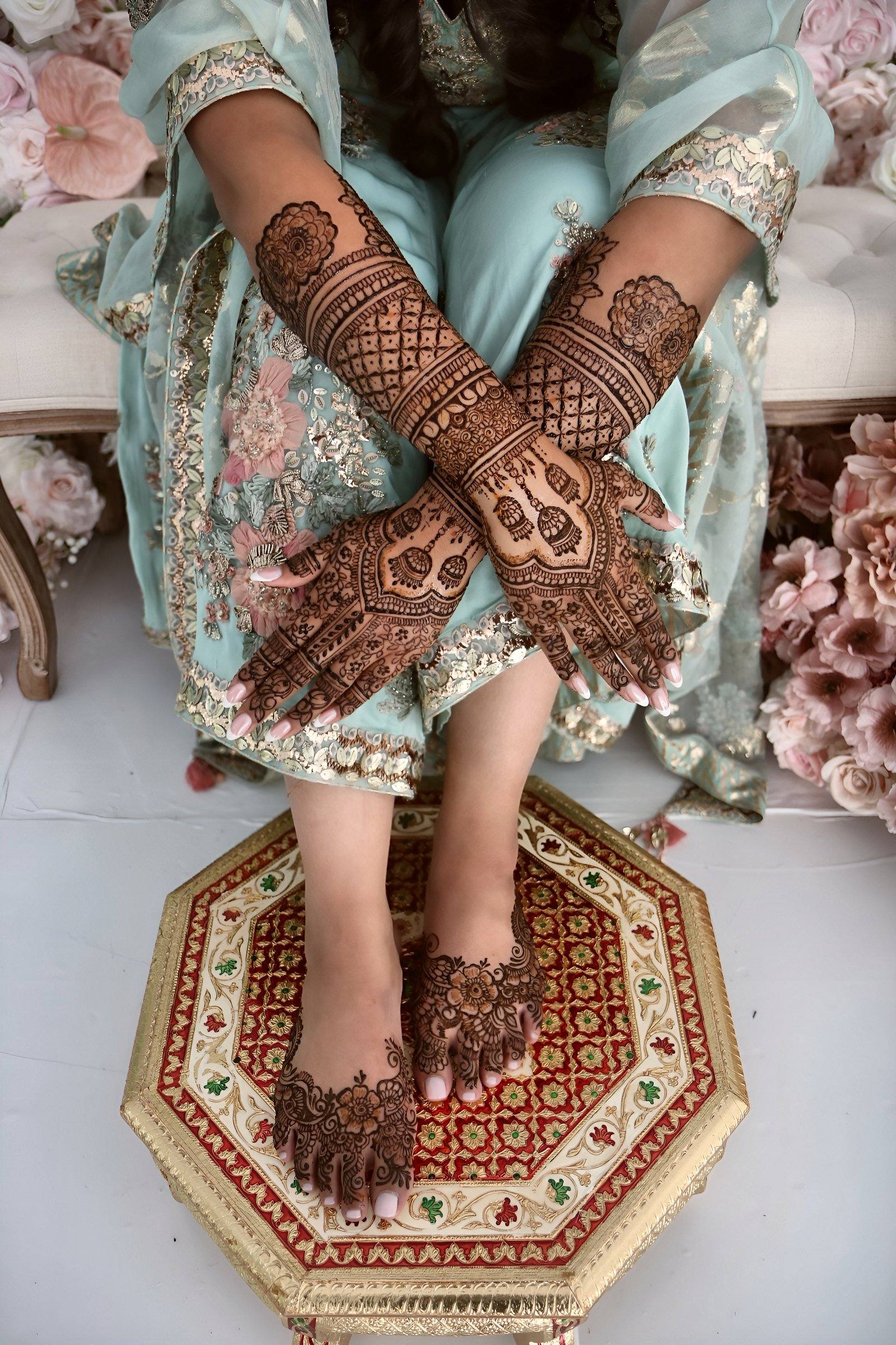 Seated bride showing henna on hands and feet on a decorative stool