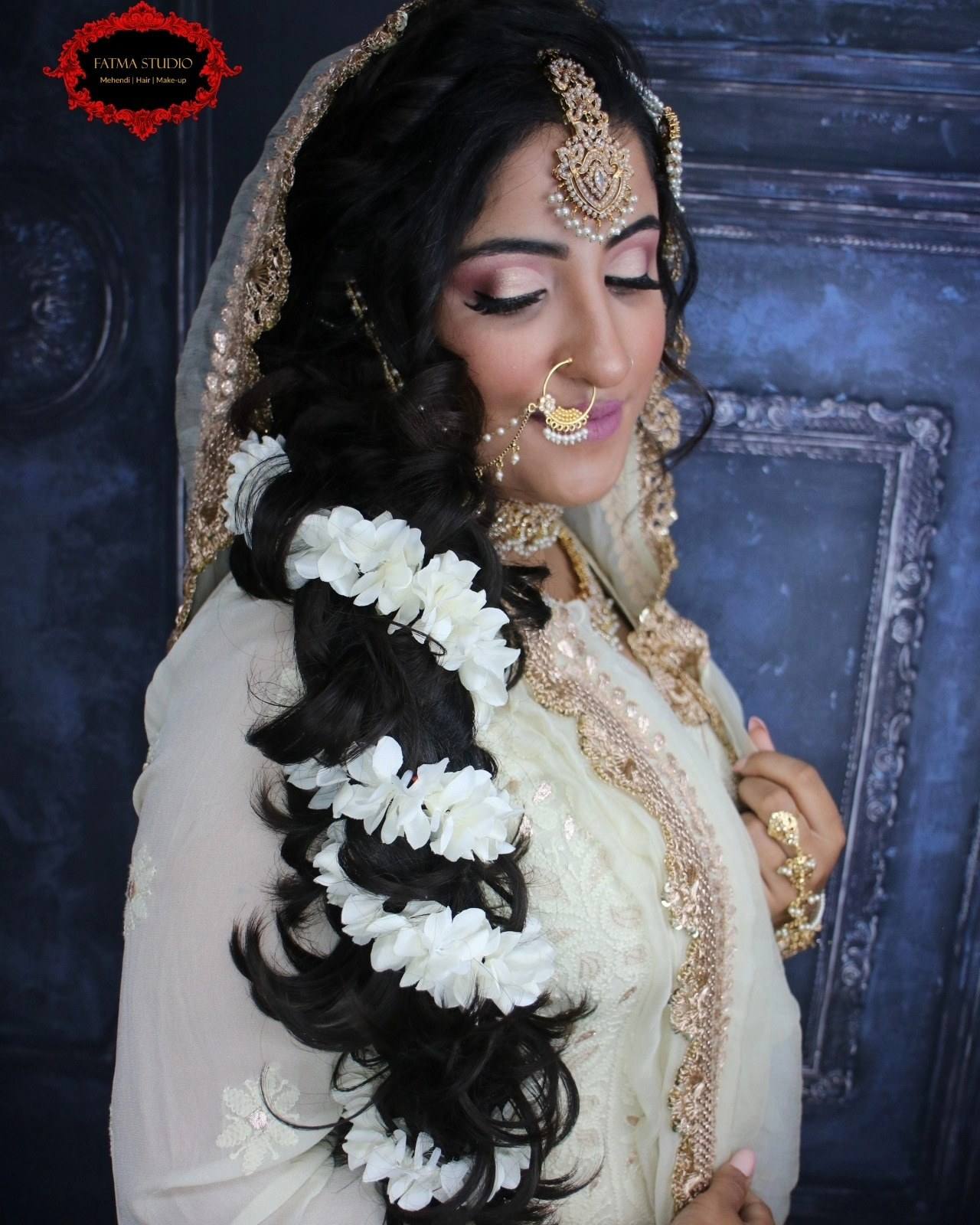 Side profile of a bride with curled hair woven with white flowers and glam makeup
